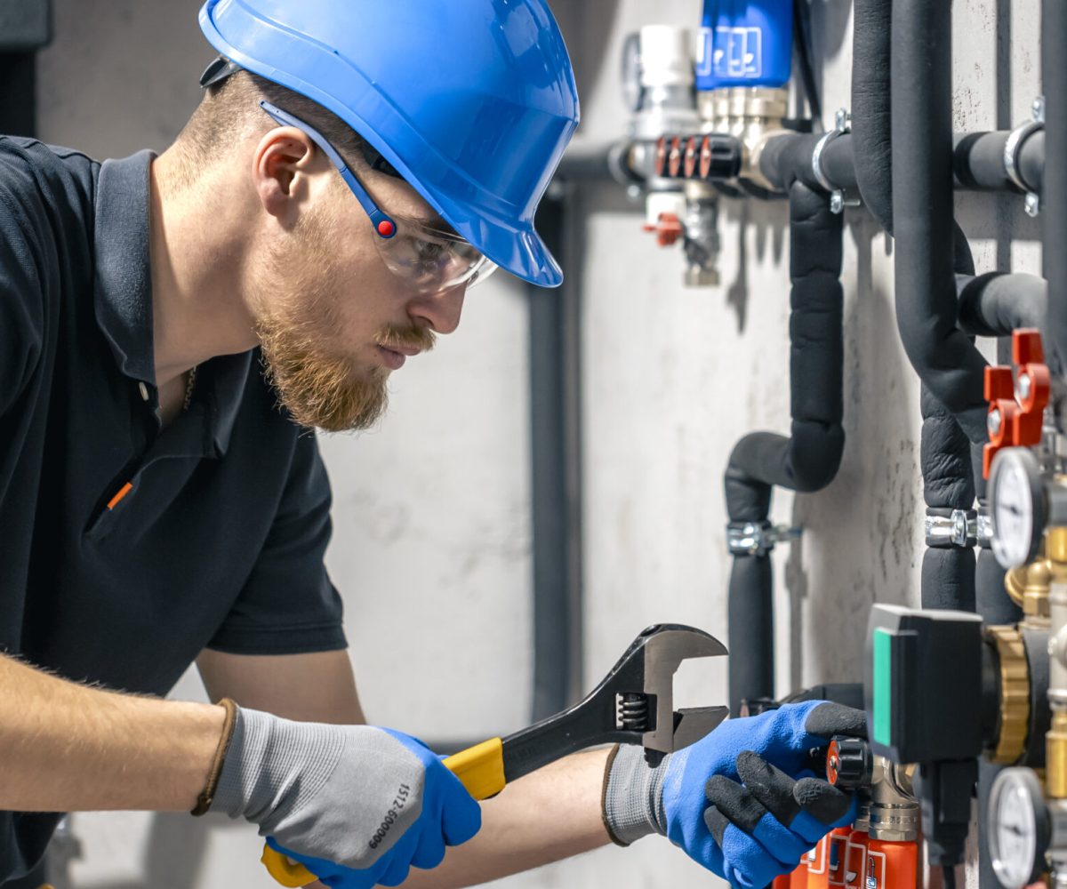 A man installs a heating system in a house and checks the pipes with a wrench. Adjusting heating valves in a residential building. A plumbing and heating technician works.